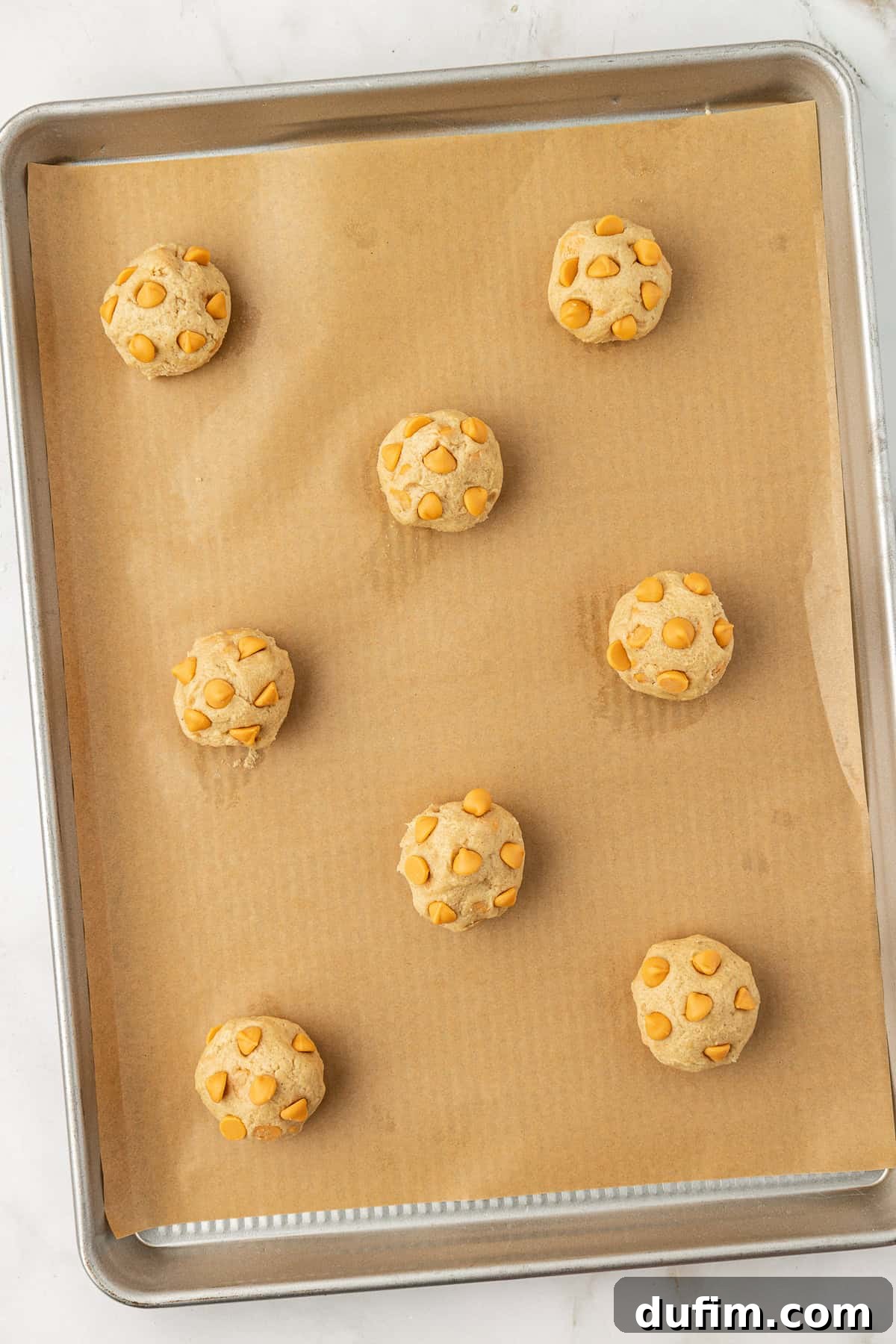 Sweet Butterscotch Chip Delights 13 Overhead view of perfectly formed butterscotch cookie dough balls, ready for baking, arranged on a baking sheet lined with parchment paper.