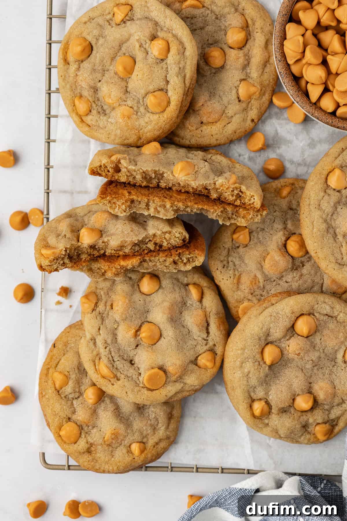 Sweet Butterscotch Chip Delights 3 Overhead view of a pile of golden-brown butterscotch cookies cooling on a wire rack lined with white parchment paper, surrounded by a bowl of butterscotch chips and scattered chips.