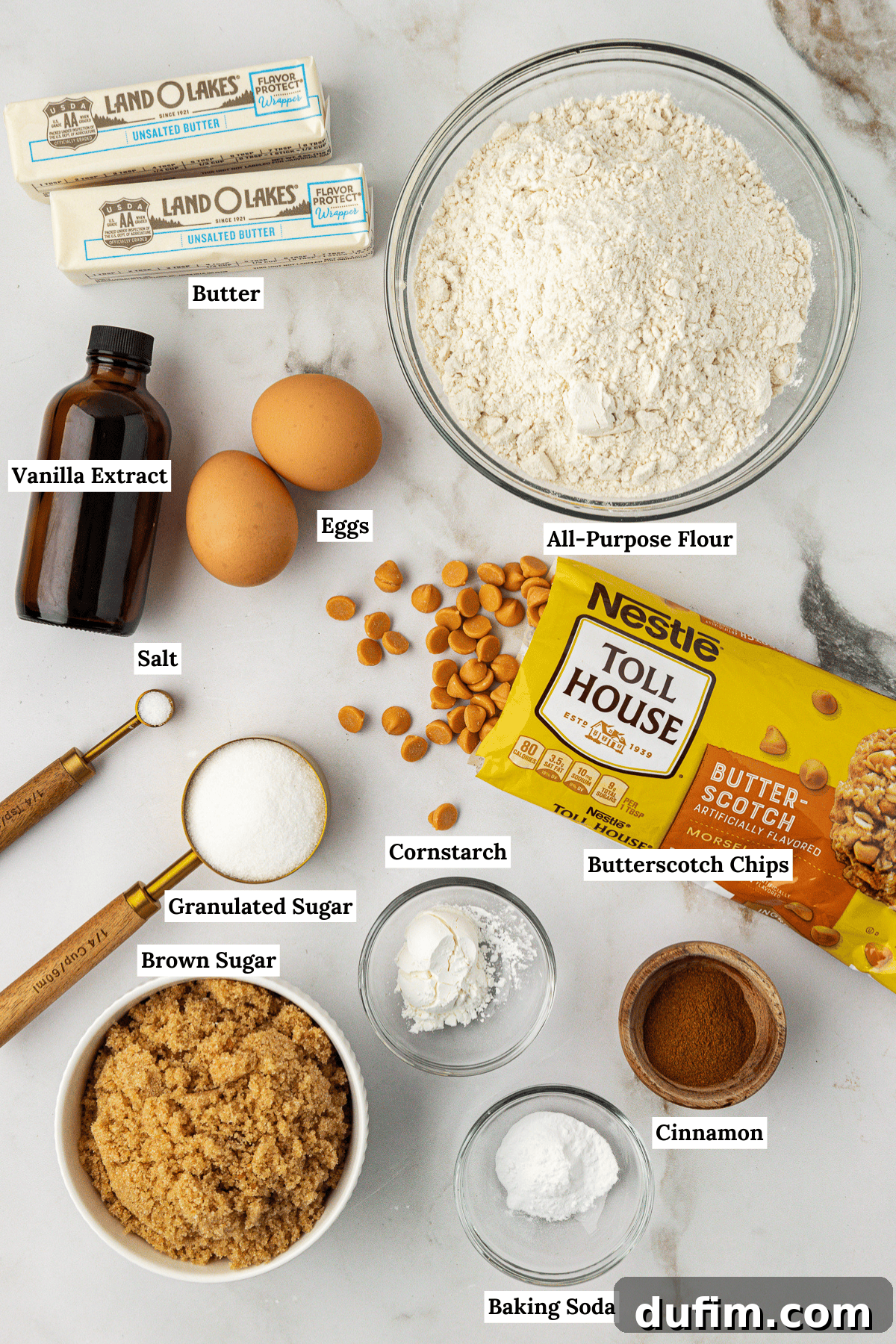 Sweet Butterscotch Chip Delights 4 Overhead view of all the fresh ingredients for butterscotch cookies arranged on a surface: butter, vanilla extract, eggs, all-purpose flour, salt, granulated sugar, cornstarch, butterscotch chips, brown sugar, baking soda, and cinnamon.