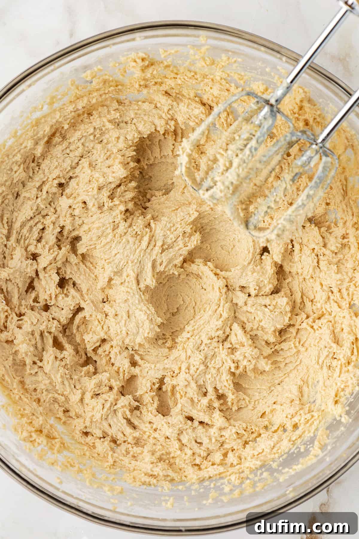 Sweet Butterscotch Chip Delights 8 Wet ingredients for butterscotch cookies, including creamed butter and sugars, mixed together in a clear glass bowl with an electric mixer resting on the side, showing a light and fluffy texture.