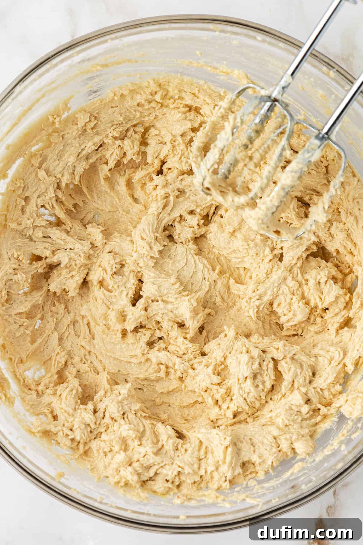 Sweet Butterscotch Chip Delights 10 Butterscotch cookie dough being thoroughly mixed with an electric mixer in a clear glass bowl, achieving a smooth and uniform consistency.