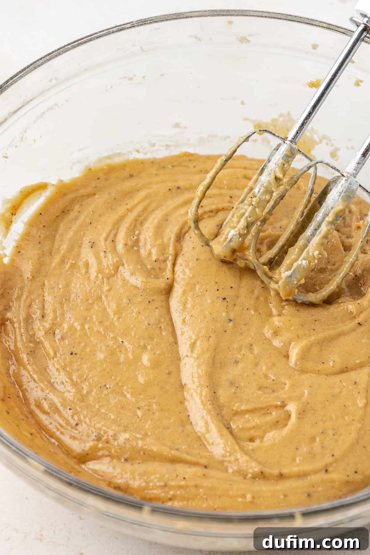 Golden Blondie Bars 12 Thick, golden blondie batter thoroughly mixed in a clear glass bowl, with an electric mixer resting on the side, ready for baking.