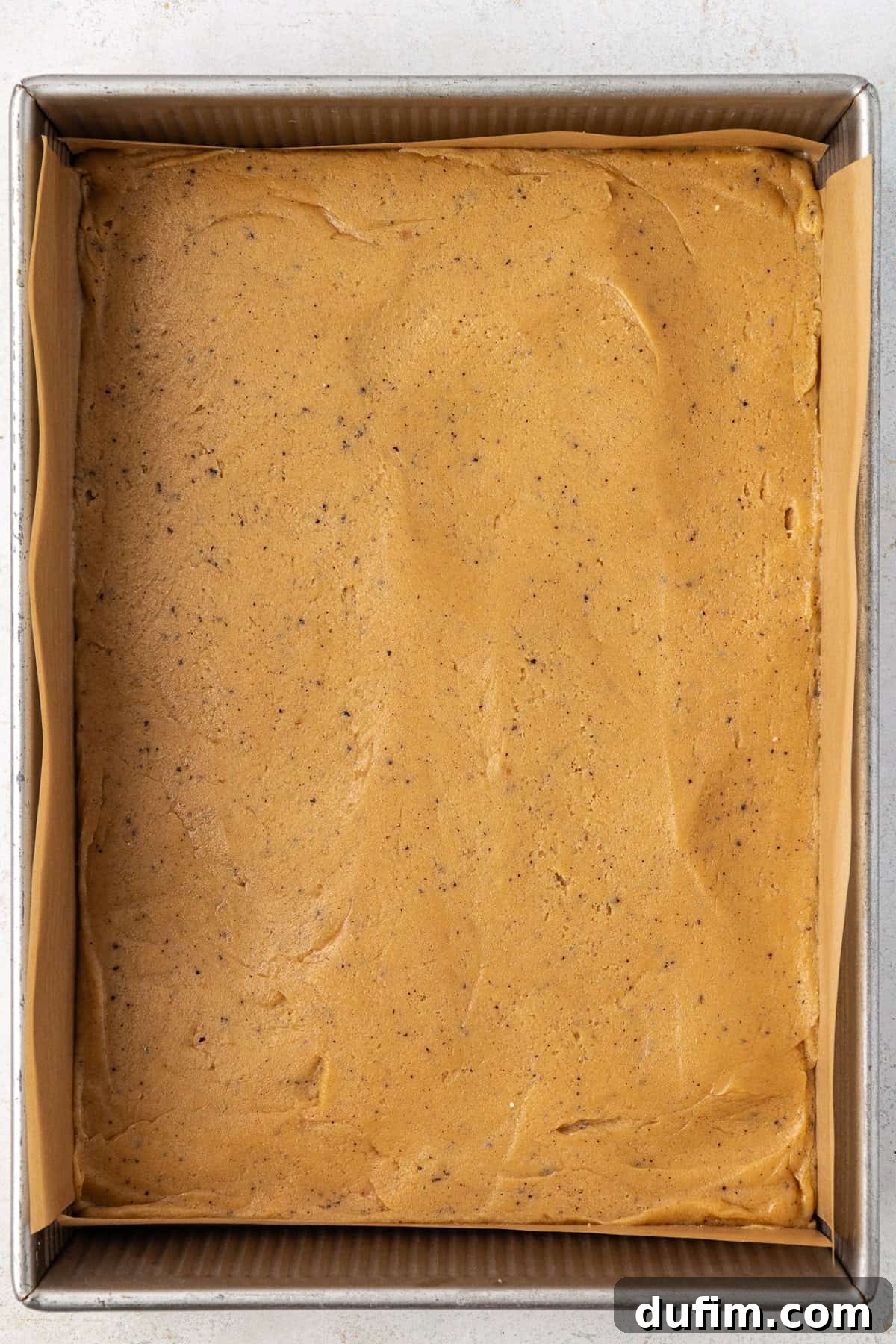 Golden Blondie Bars 13 A metal baking pan, neatly lined with parchment paper, filled with the rich, golden blondie batter, smoothed evenly and ready for the oven.