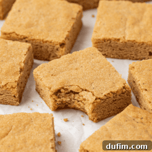 Close-up of golden blondies scattered on white parchment paper, with a delightful bite taken out of the center blondie.