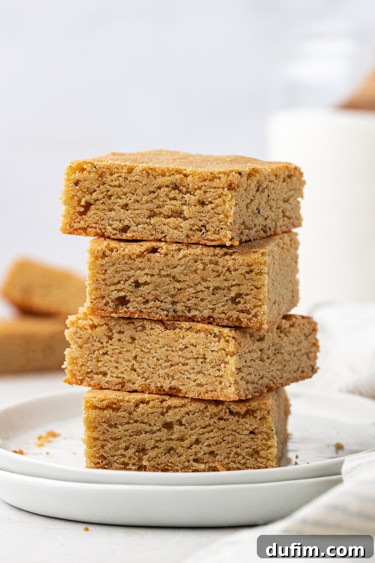 Golden Blondie Bars 3 A stack of four golden-brown blondies presented on two small white plates, highlighting their thickness and appealing texture.