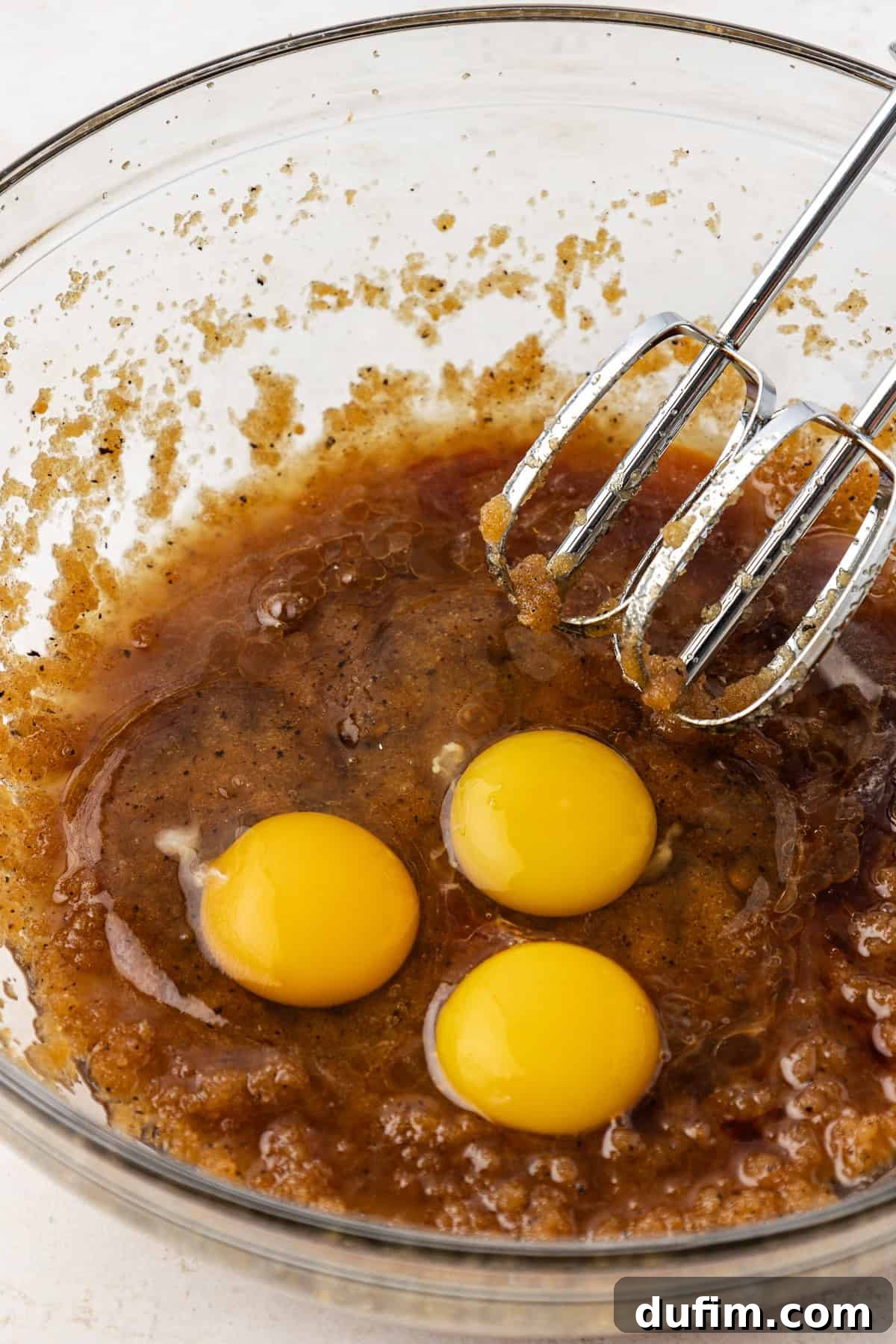 Golden Blondie Bars 10 The wet ingredients for blondies, including three eggs on top, in a clear glass bowl with an electric mixer poised to combine them.
