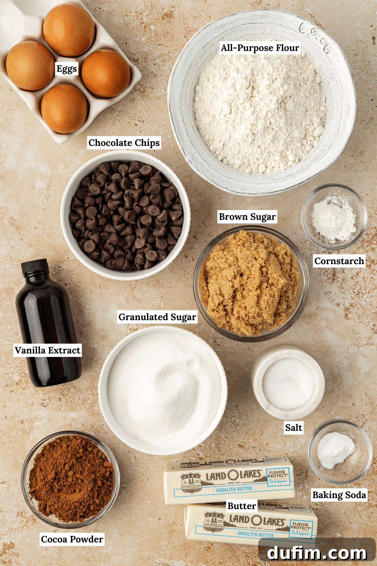 An overhead view of all the essential ingredients laid out for making brookies, including fresh eggs, all-purpose flour, an abundance of chocolate chips, vanilla extract, brown sugar, cornstarch, granulated sugar, rich cocoa powder, softened butter, salt, and baking soda, neatly arranged on a clean kitchen surface, ready for baking.
