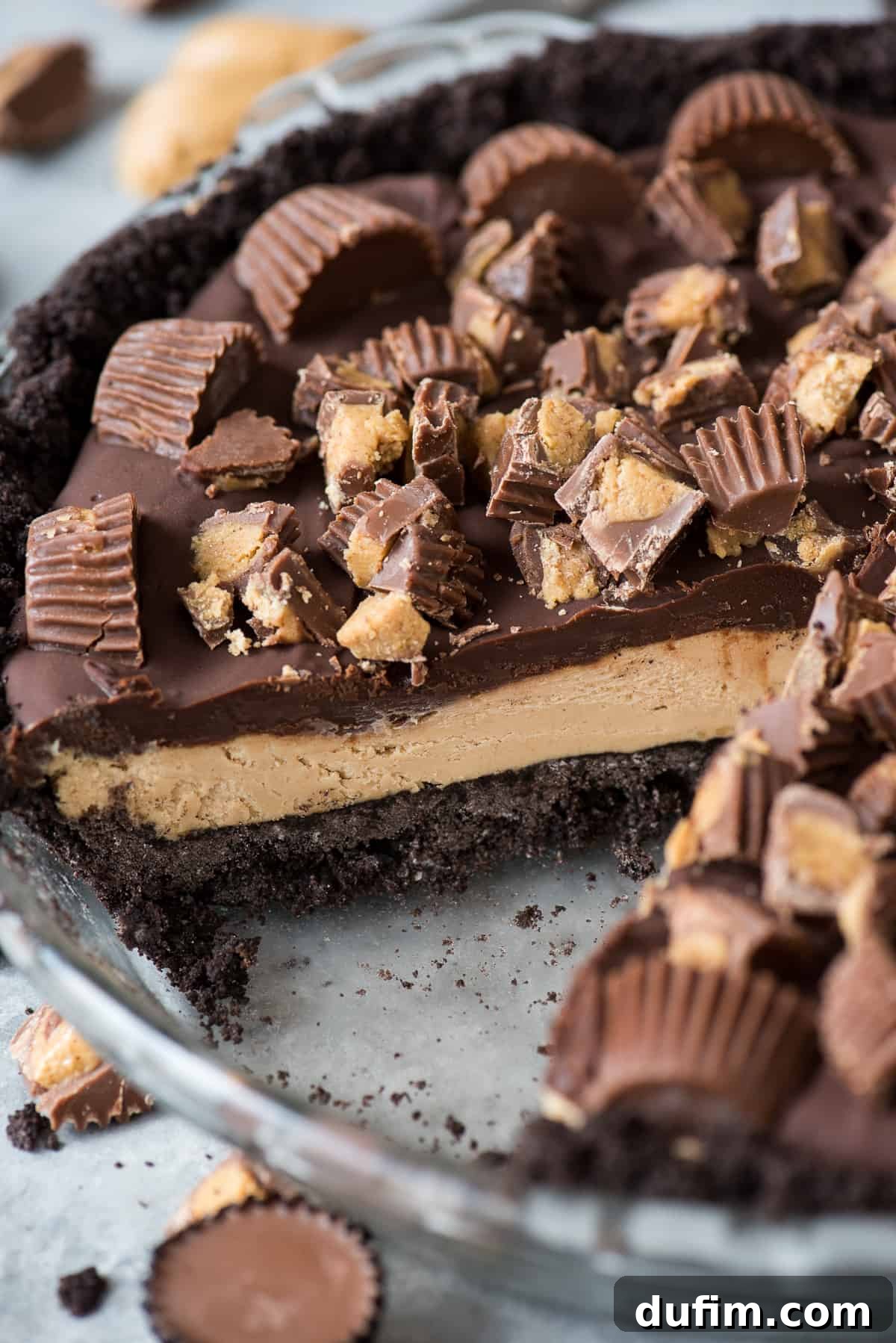 A visually appealing chocolate peanut butter pie with Reese's cups in a glass pie pan, with one slice already removed, highlighting its tempting layers and perfect presentation.