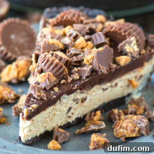 A beautifully presented slice of chocolate peanut butter cheesecake, generously topped with an array of whole and chopped Reese's peanut butter cups, artfully arranged on a gray plate, evoking pure dessert bliss.