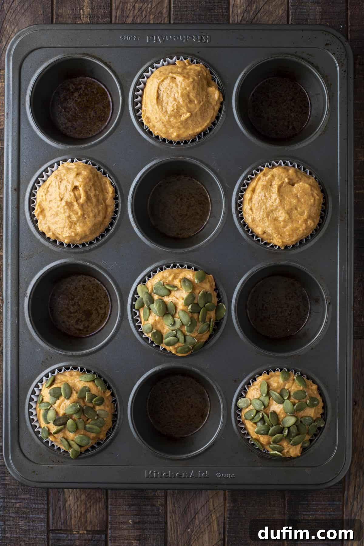 healthy pumpkin muffin batter in every other hole of a muffin pan with 3 topped with pumpkin seeds and 3 without