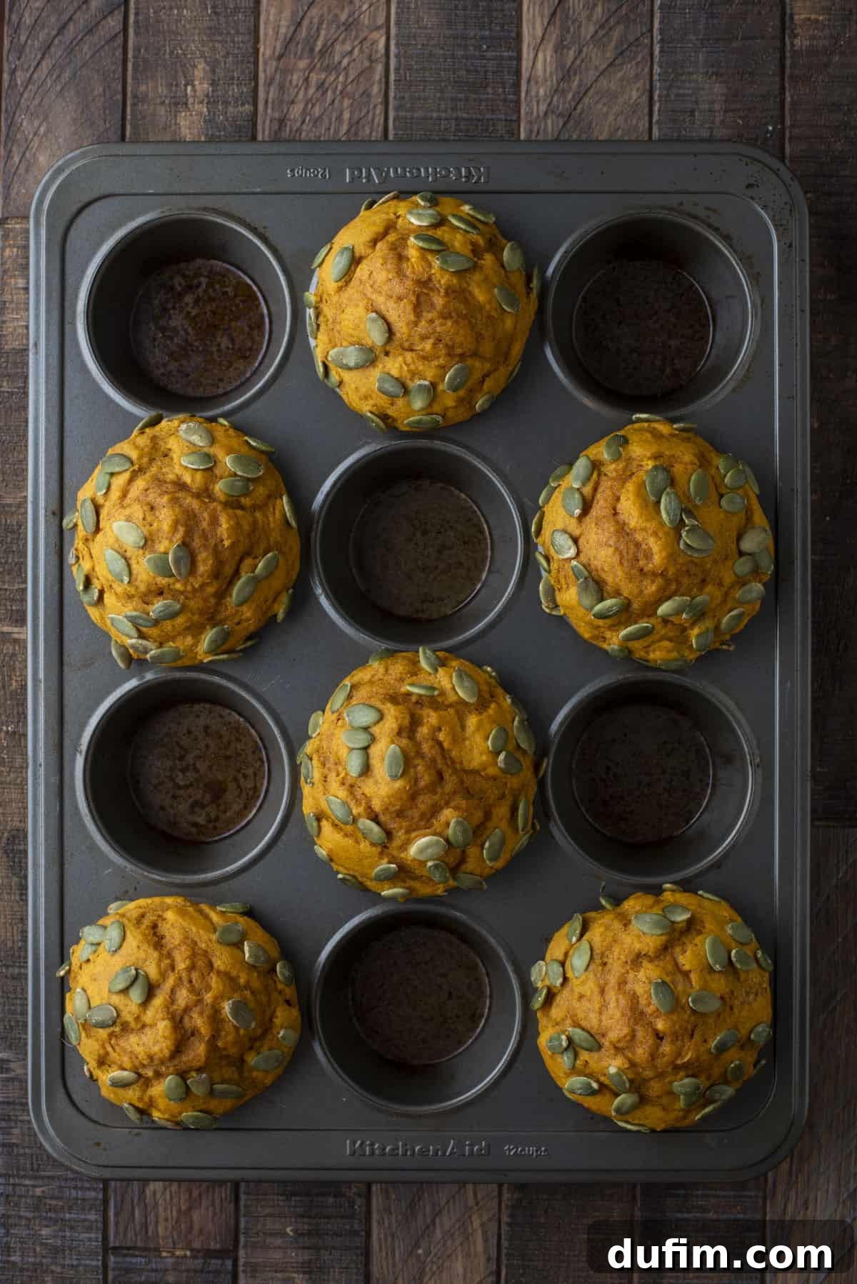 freshly baked pumpkin muffins topped with pumpkin seeds in every other hole of a muffin pan
