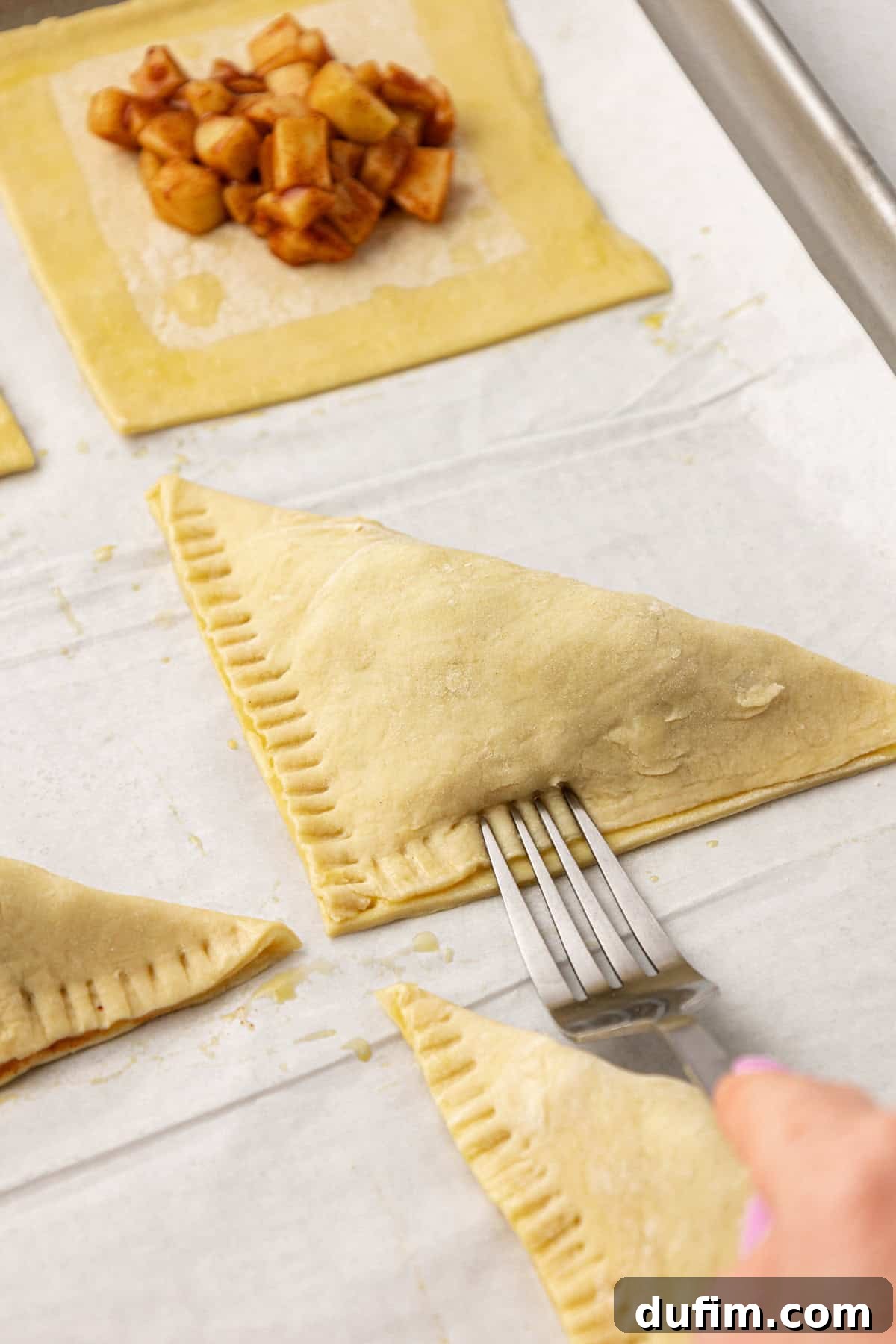 Golden Flaky Apple Turnovers 11 A fork firmly crimping the edges of an apple turnover, creating a beautiful sealed pattern.