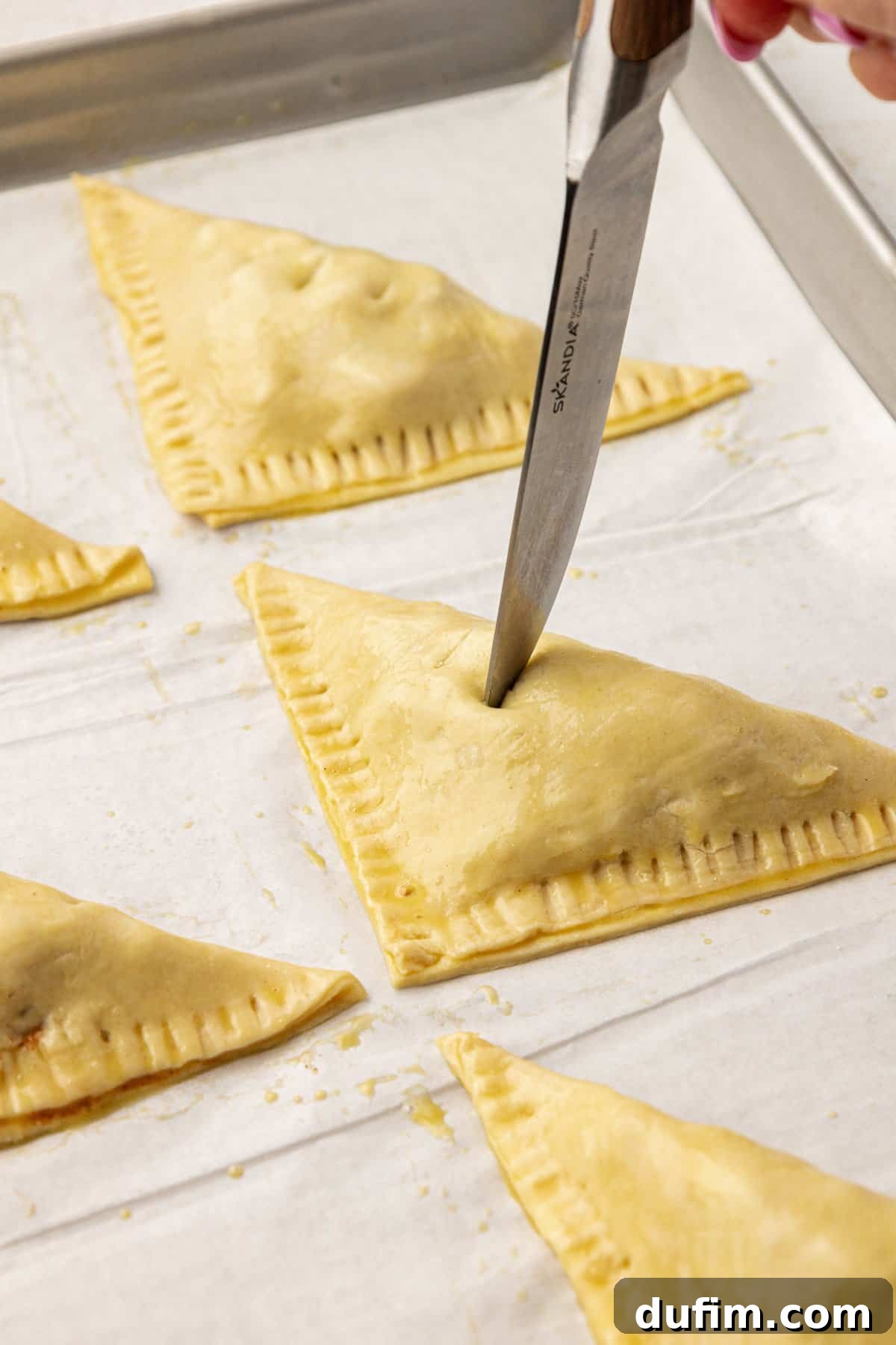 Golden Flaky Apple Turnovers 12 A sharp knife carefully making two vent slits on the top of an assembled apple turnover, crucial for even baking.
