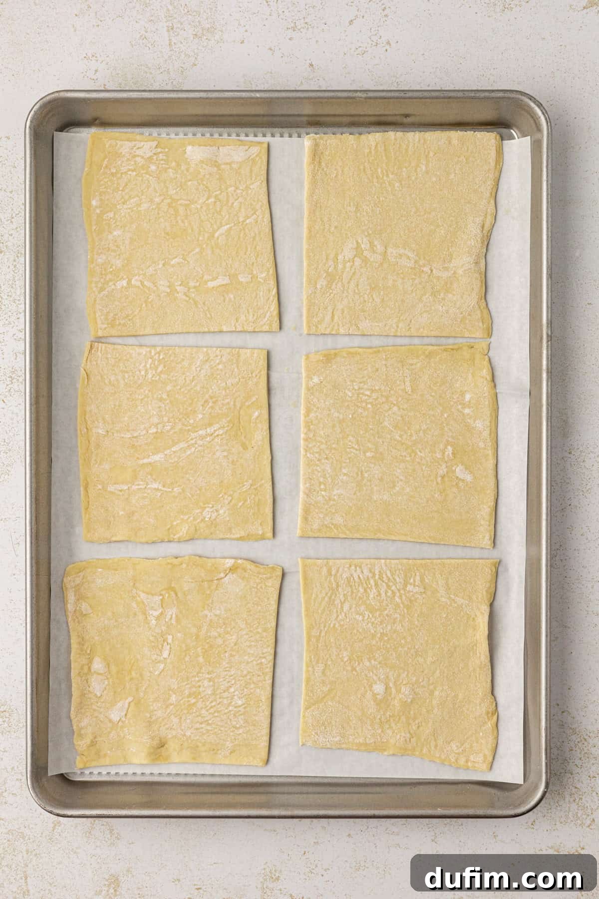 Golden Flaky Apple Turnovers 7 Six evenly cut puff pastry squares arranged on a baking sheet lined with parchment paper, perfectly prepped for filling.
