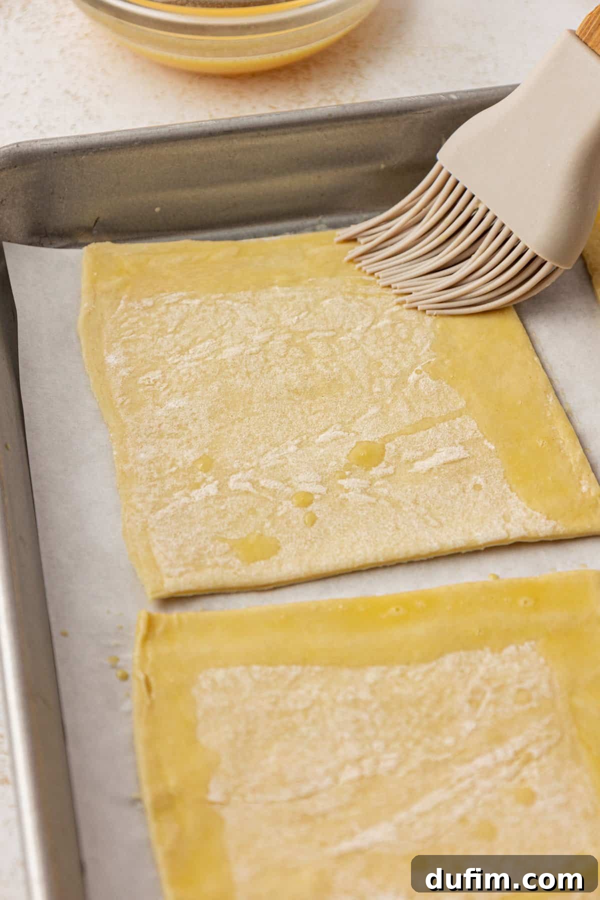 Golden Flaky Apple Turnovers 8 A pastry brush applying a glistening egg wash along the edges of puff pastry squares, preparing them for sealing.