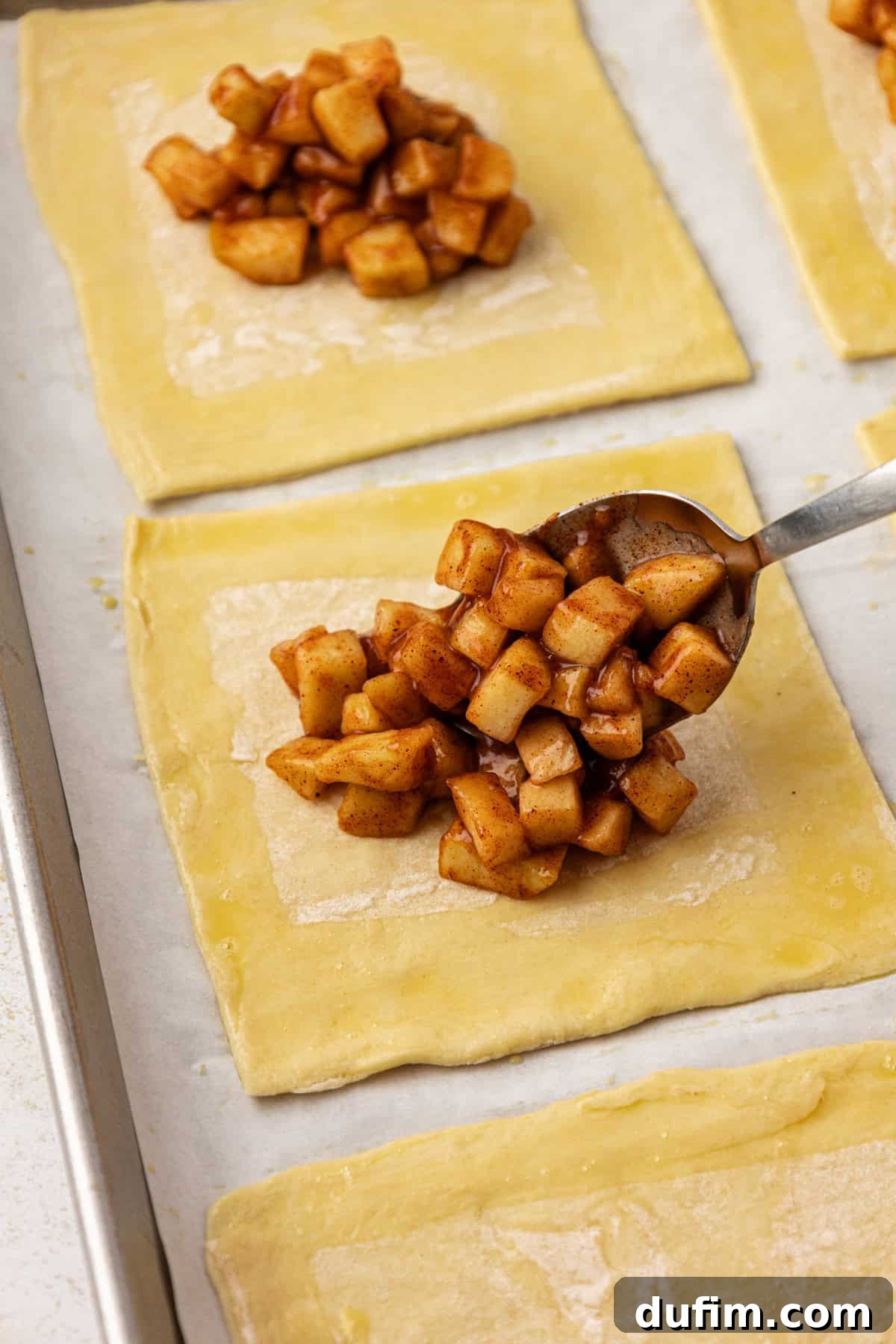 Golden Flaky Apple Turnovers 9 A generous spoonful of spiced apple filling being placed onto the center of a puff pastry square, ready for folding.