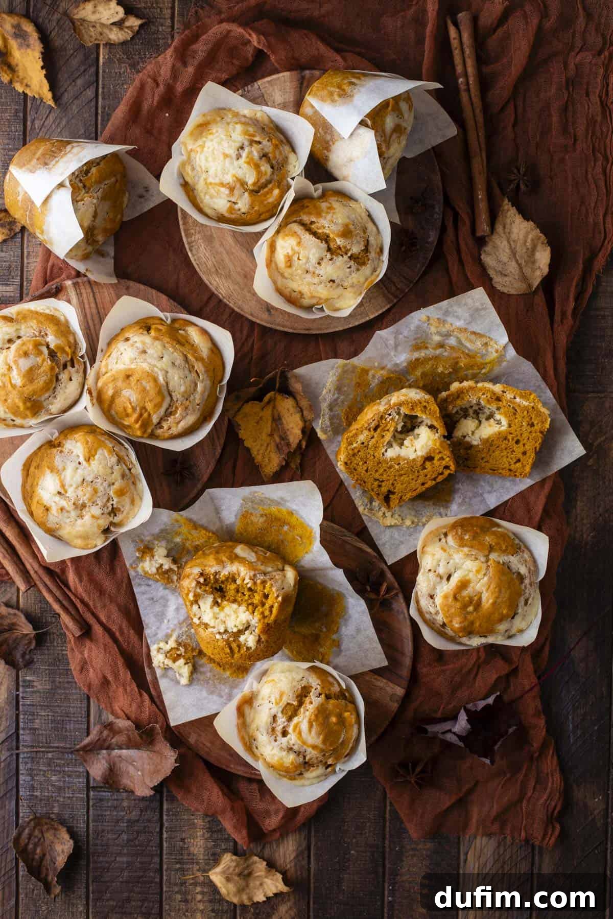 overhead view of pumpkin cream cheese muffins scattered around, some upright, some on their sides cut in half, some with a bite missing, with fall leaves scattered around