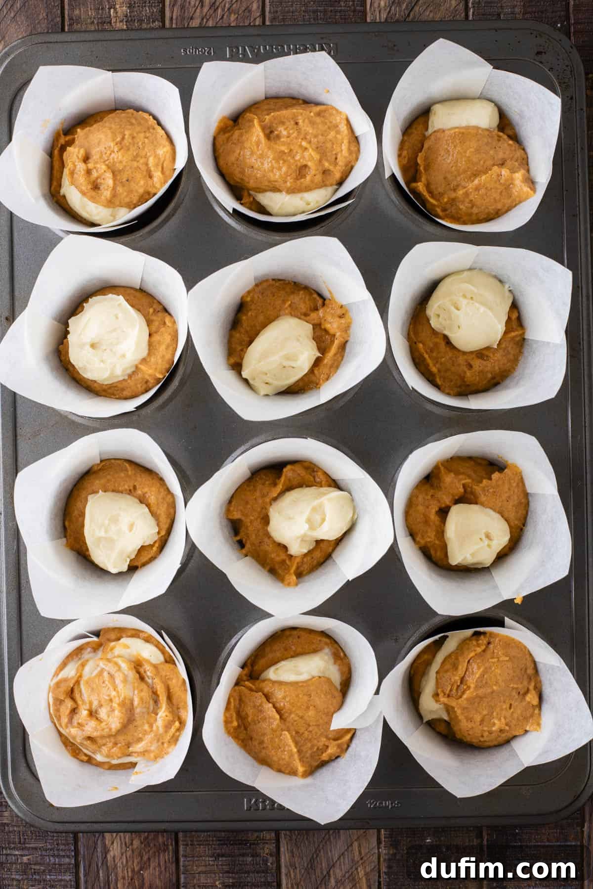 over head view of pumpkin muffin batter and cream cheese mixture layered in muffin liners in a muffin pan