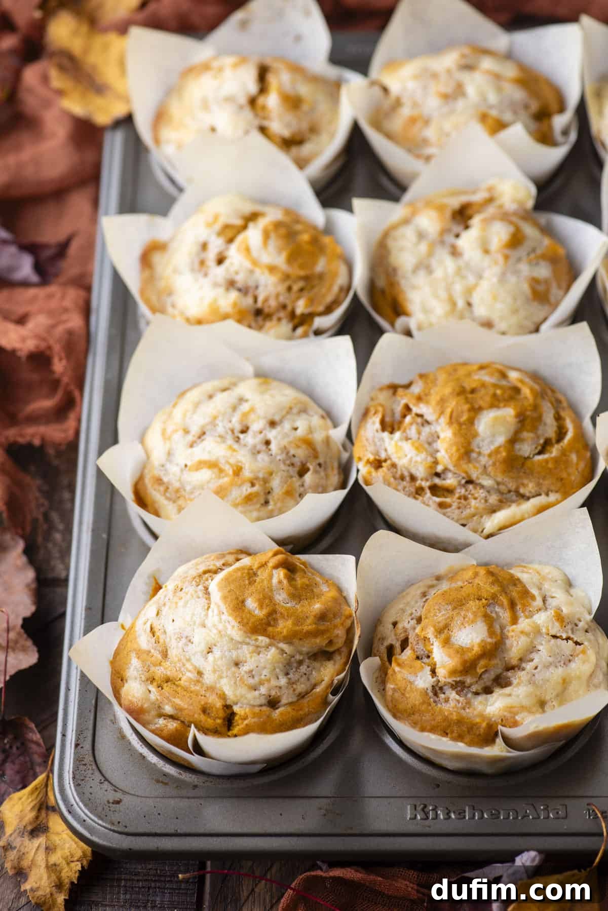 a muffin pan full of pumpkin cream cheese muffins in white liners