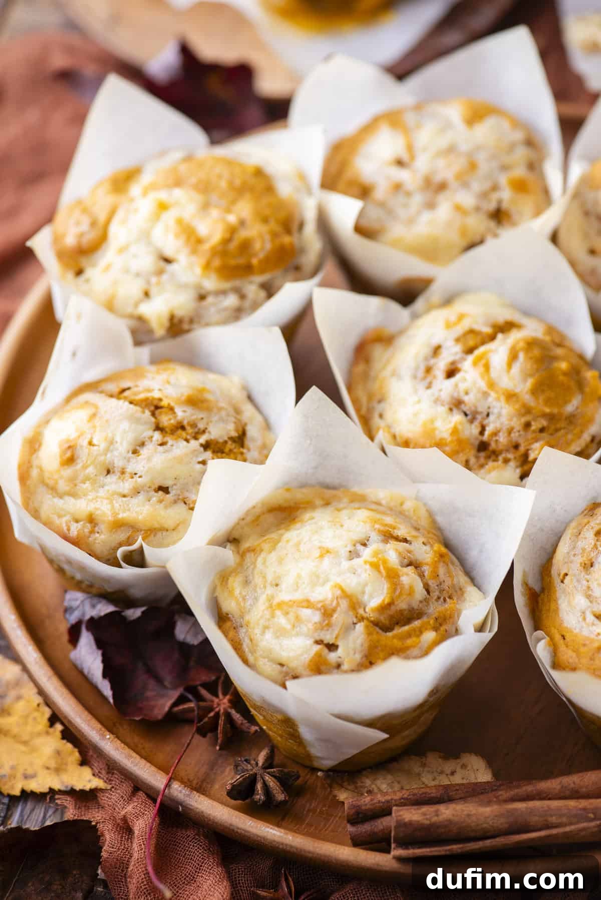 pumpkin cream cheese muffins in paper muffin cups on a wood platter surrounded by fall leaves