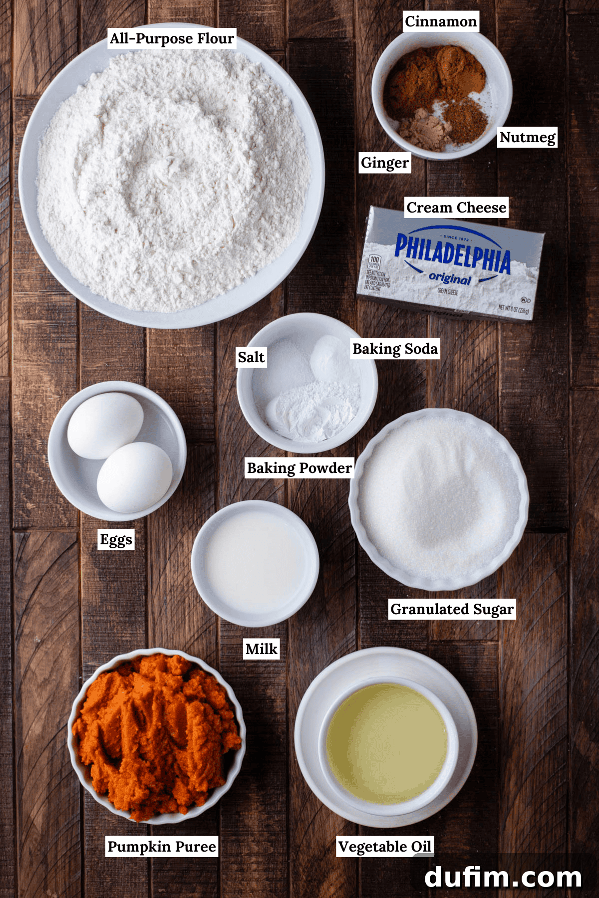 overhead view of the ingredients for pumpkin cream cheese muffins including all-purpose flour, cinnamon, ginger, nutmeg, cream cheese, eggs, salt, baking soda, granulated sugar, milk, pumpkin puree, and vegetable oil