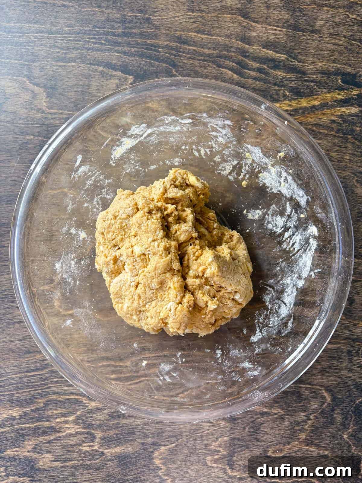 Overhead view of pumpkin scone dough inside a clear glass bowl, showcasing its thick and slightly sticky consistency. The ingredients are just combined, indicating proper mixing without overworking, essential for tender, flaky scones.