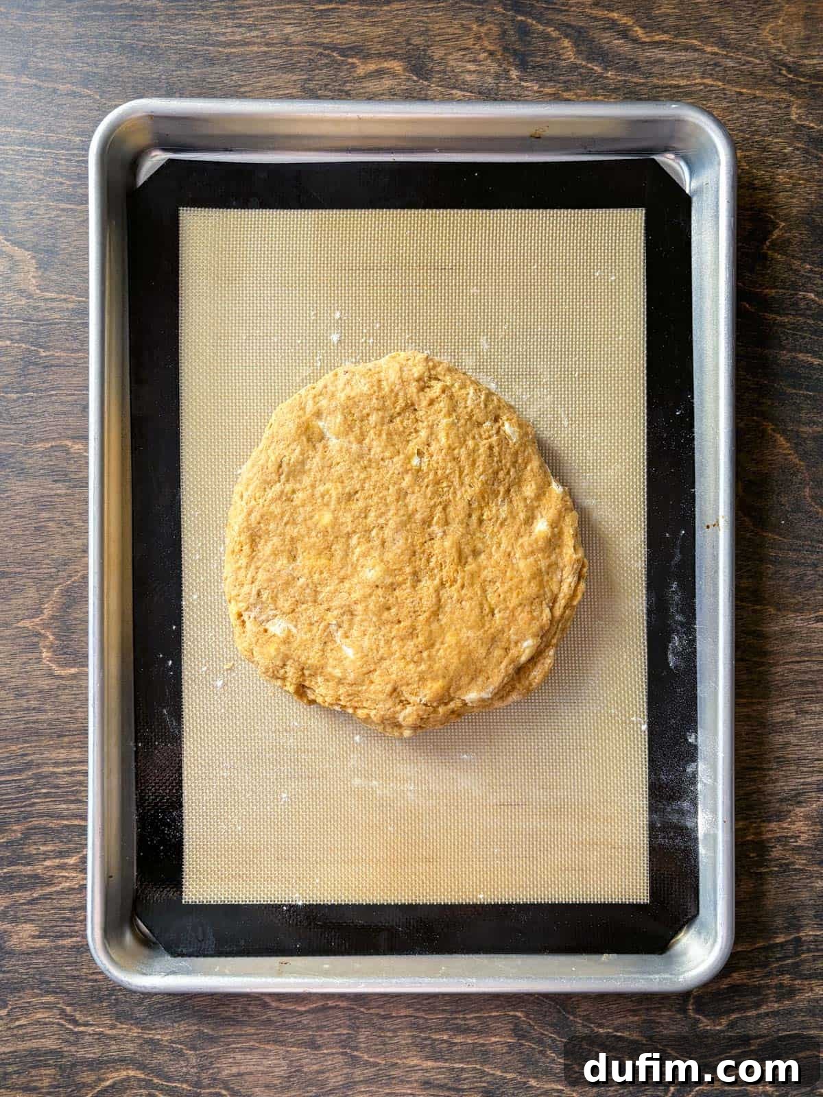 Overhead view of a perfectly shaped circle of pumpkin scone dough resting on a baking sheet lined with a silicone mat, ready for chilling and cutting. The smooth, even surface of the dough indicates it's well-prepared for the next steps in creating delicious, bakery-style scones.