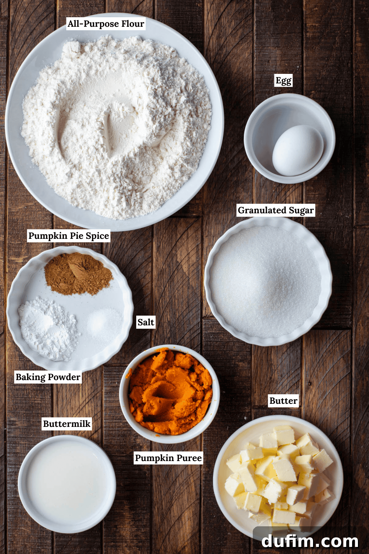 Overhead view of the carefully arranged ingredients for pumpkin scones, including vibrant orange pumpkin puree, creamy buttermilk, golden egg, cubed cold butter, and a precise blend of dry ingredients like all-purpose flour, granulated sugar, baking powder, pumpkin pie spice, and salt, ready for mixing.