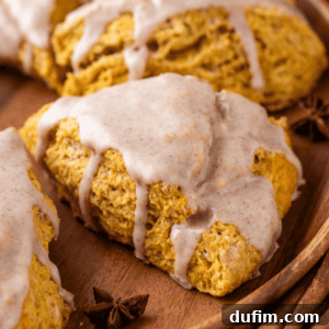 Close-up of a perfectly baked pumpkin scone on a rustic wood plate, with a delicate star anise pod resting beside it. The scone's golden-brown crust and soft interior promise a delicious fall treat.