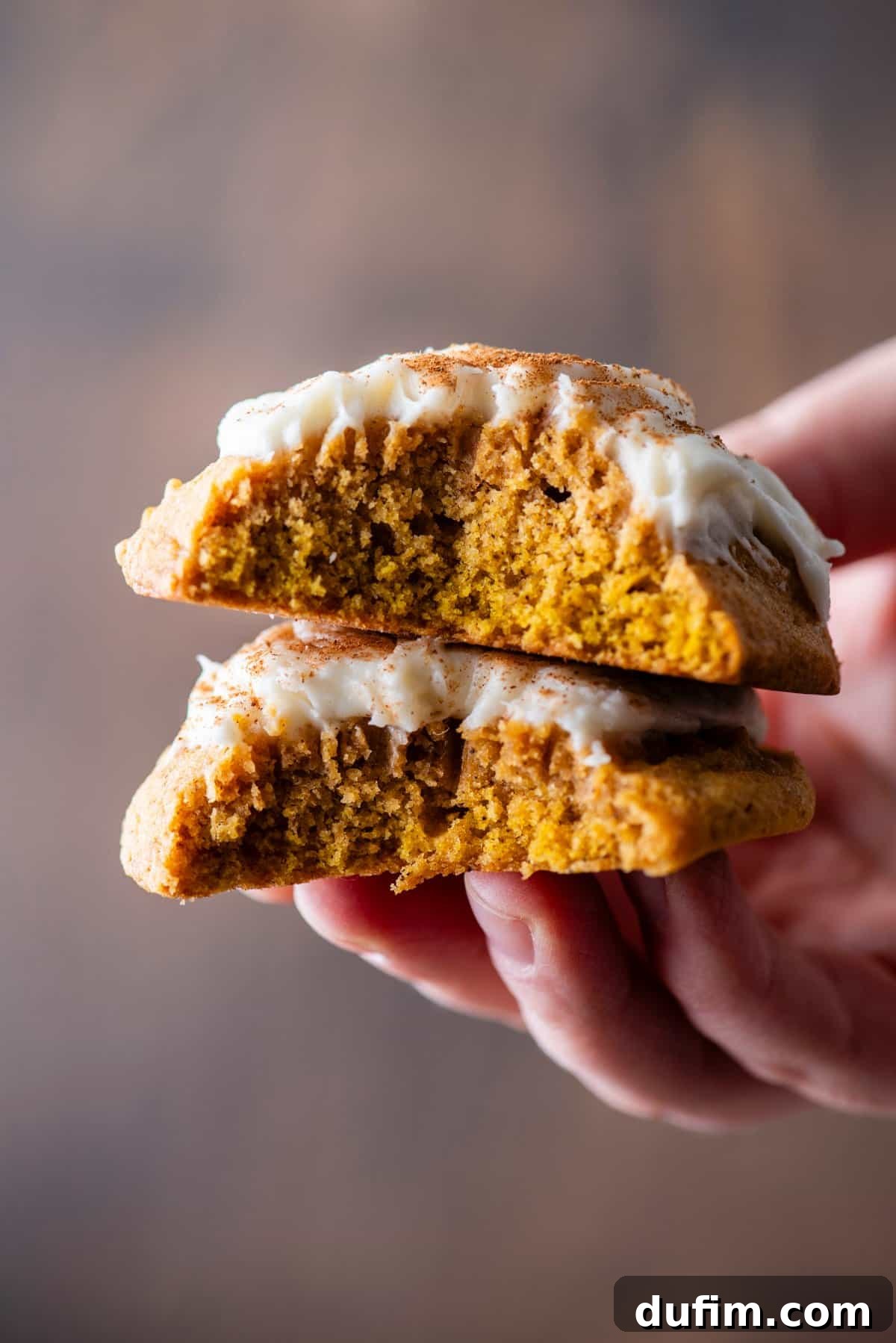 Cozy Autumn Pumpkin Spice Cookies 3 a hand holding a pumpkin cookie split in half and stacked together, showing the layers of cookie and cream cheese frosting