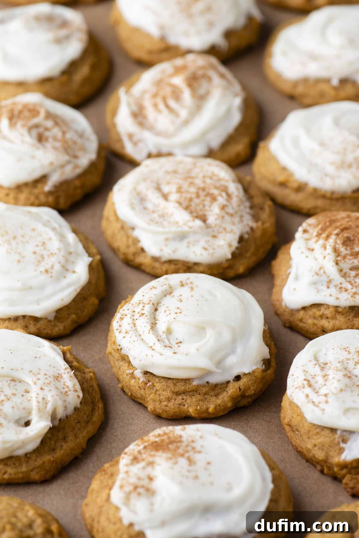 Cozy Autumn Pumpkin Spice Cookies 5 rows of pumpkin cookies with cream cheese frosting on brown parchment paper