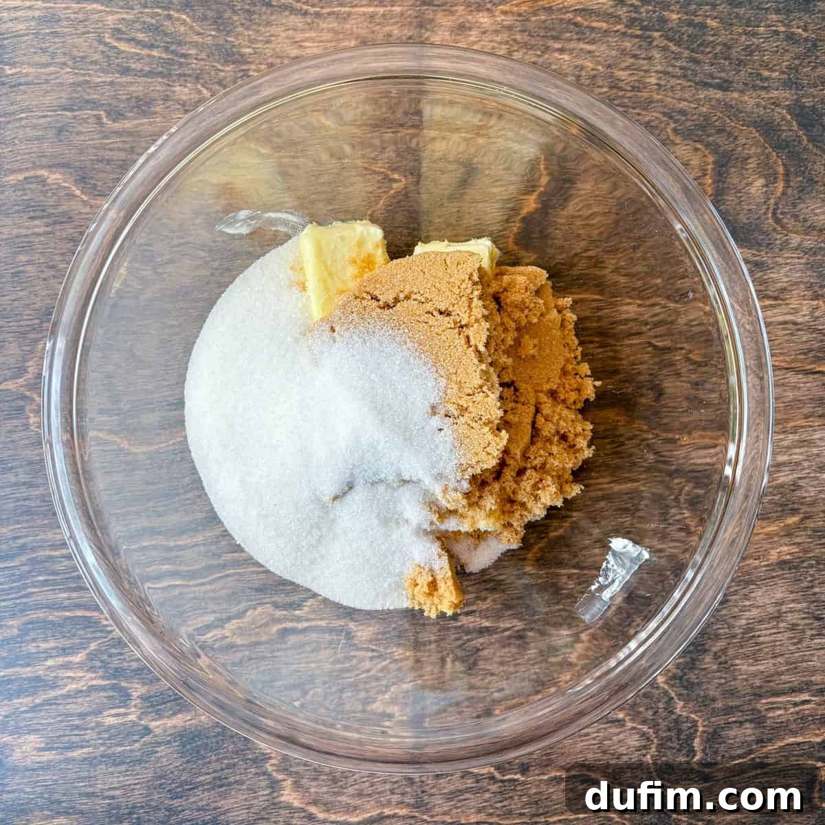 Cozy Autumn Pumpkin Spice Cookies 7 over head view of a clear glass bowl on a wood surface, with granulated sugar, brown sugar and butter in it