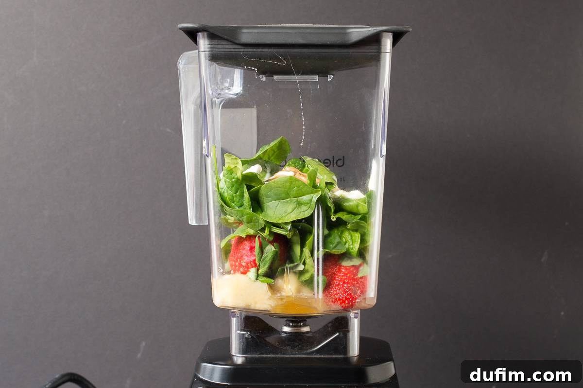 All the ingredients for spinach muffins, including bananas, spinach, and strawberries, are placed inside a blender, ready to be pureed into a smoothie batter.