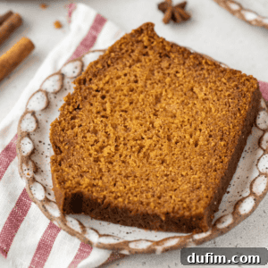 A slice of pumpkin bread on a small plate, placed on a red and white towel, surrounded by cinnamon sticks and star anise.