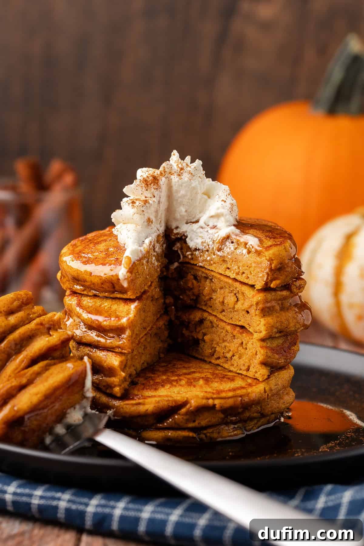 A stack of golden-brown pumpkin pancakes on a plate, with a perfect wedge missing from three layers, revealing the soft, airy interior texture.