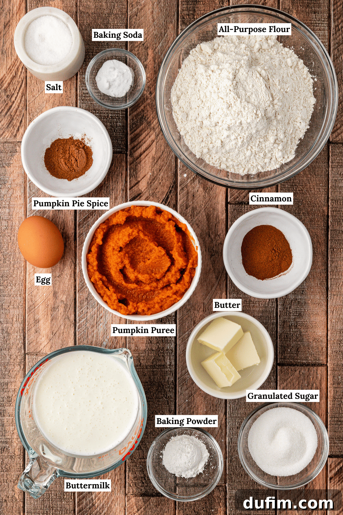 An overhead view showcasing all the essential ingredients for making delicious pumpkin pancakes, including flour, sugar, pumpkin pie spice, buttermilk, pumpkin puree, butter, and an egg, arranged beautifully on a rustic surface.