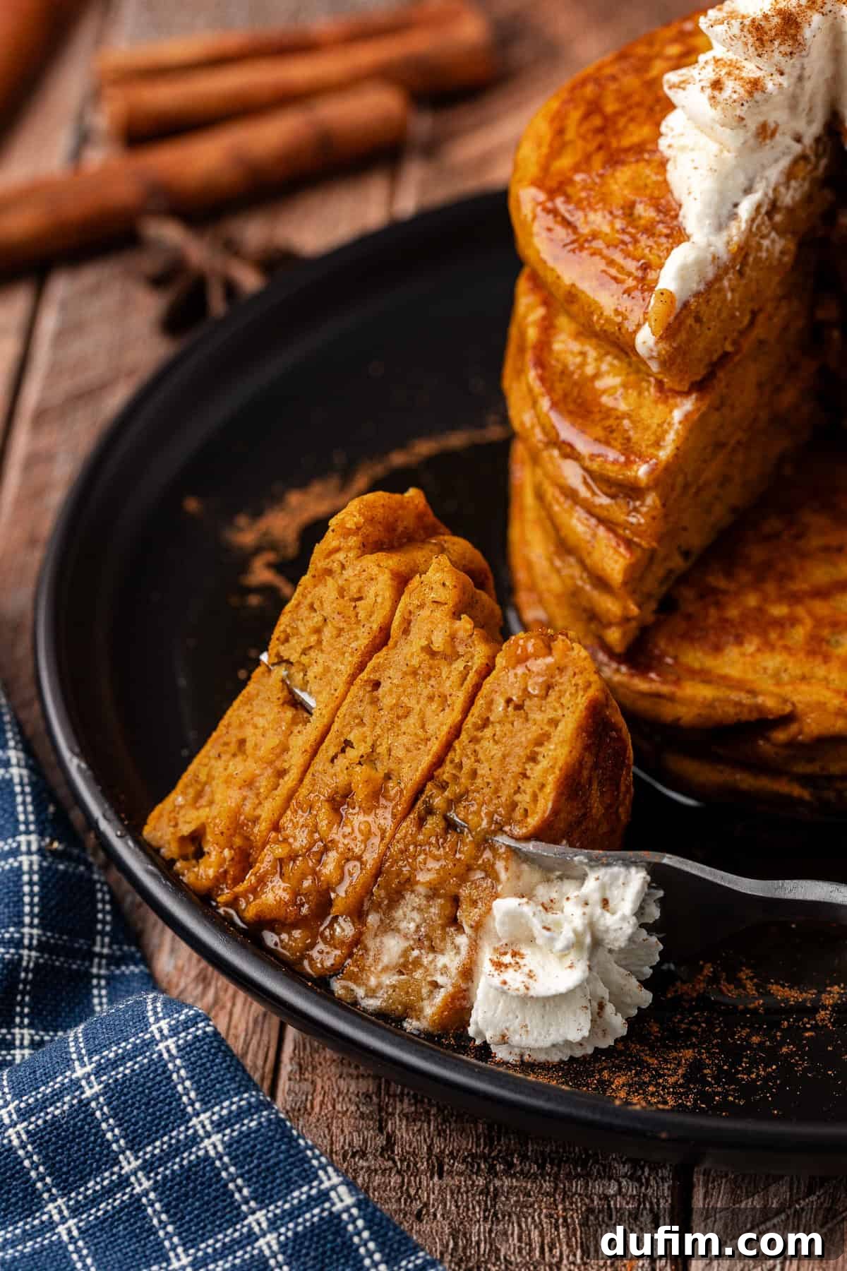 A black plate holds a neat stack of pumpkin pancakes, with a fork showcasing a perfect bite, emphasizing their delicious, golden-brown exterior and fluffy interior.