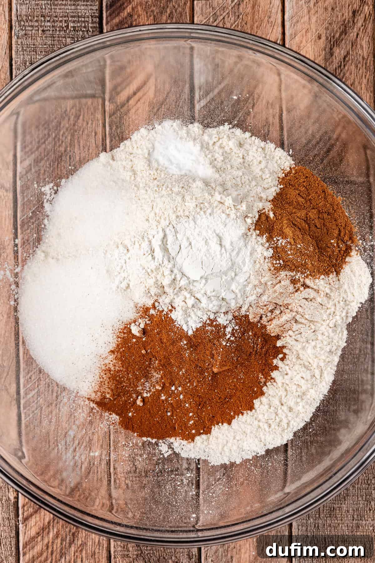 A clear glass bowl filled with the dry ingredients for pumpkin pancakes, carefully measured and ready for mixing.
