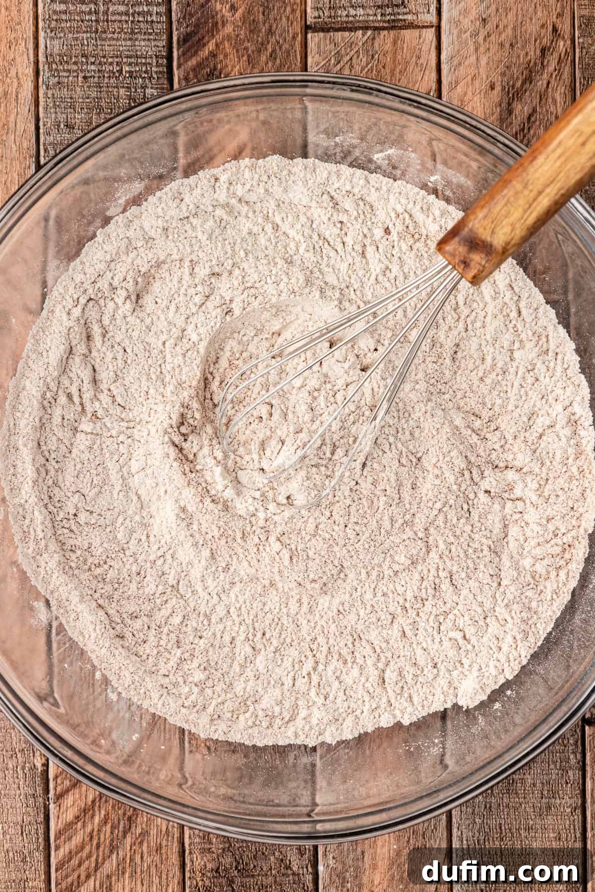 A large glass bowl containing a flour mixture, being whisked to combine the dry ingredients thoroughly for pumpkin pancakes.