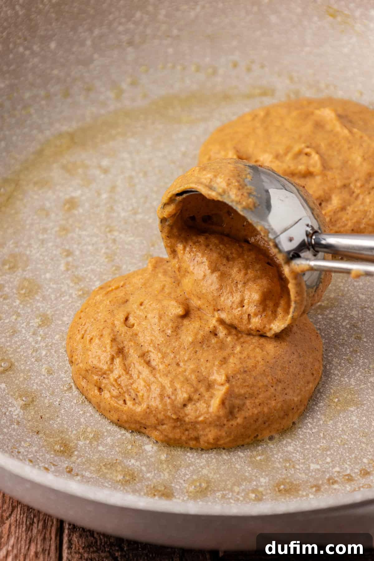 A cookie scoop carefully placing portions of pumpkin pancake batter onto a hot pan, demonstrating the start of the cooking process for perfect round pancakes.
