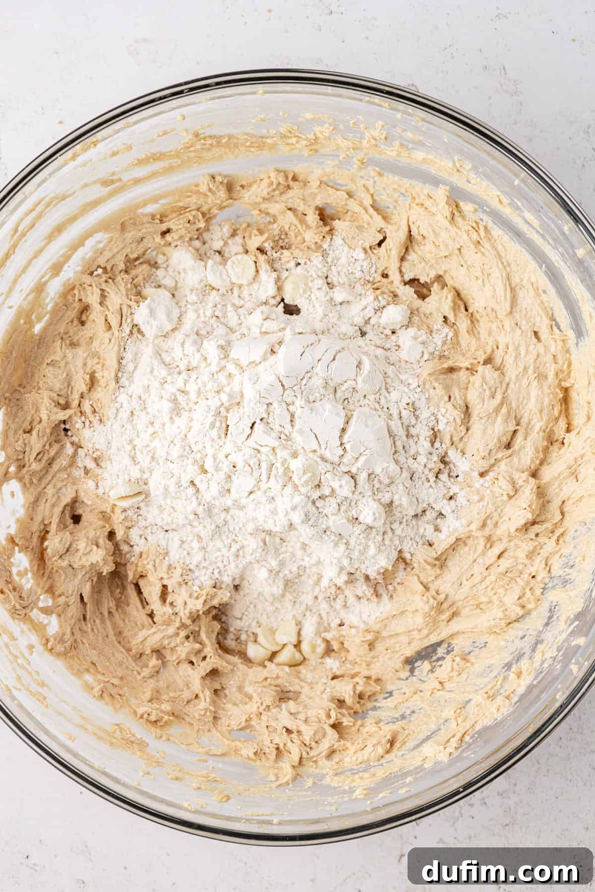 White chocolate chip cookie dough ingredients in a clear glass bowl, not yet completely combined so the flour mixture is sitting in a pile on top