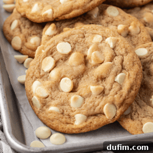 White chocolate chip cookies and white chocolate chips piled and scattered on a baking sheet