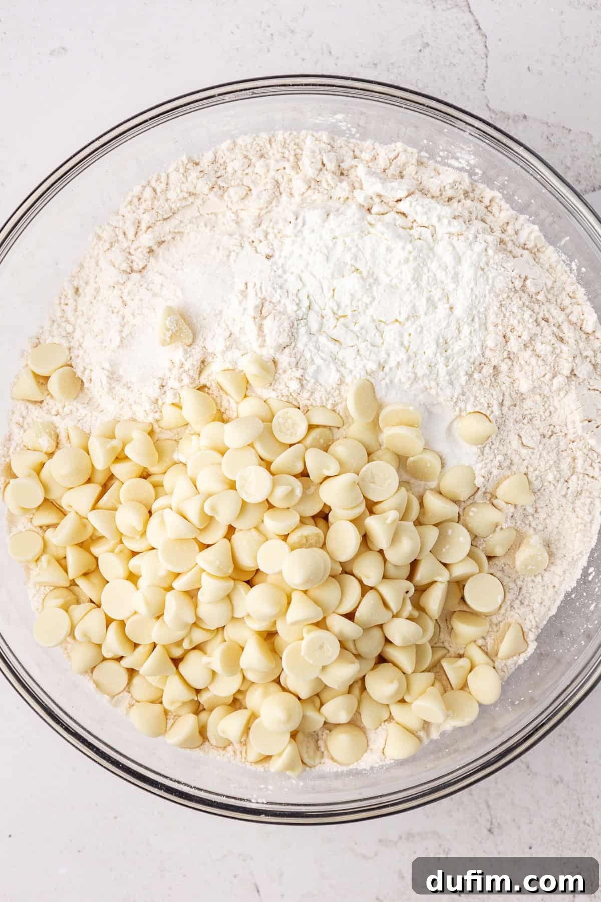 White chocolate chips and a flour mixture in a large glass bowl