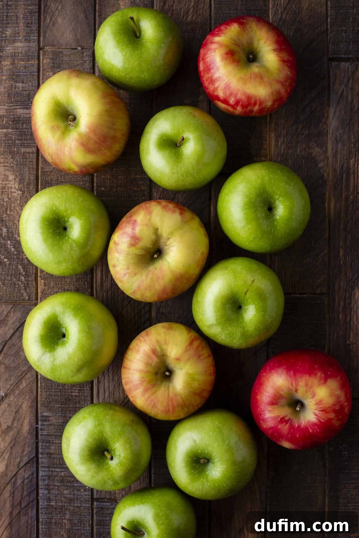 An inviting overhead view of a vibrant assortment of green and red apples, freshly harvested and artfully arranged on a warm wooden surface, ready for peeling and slicing.
