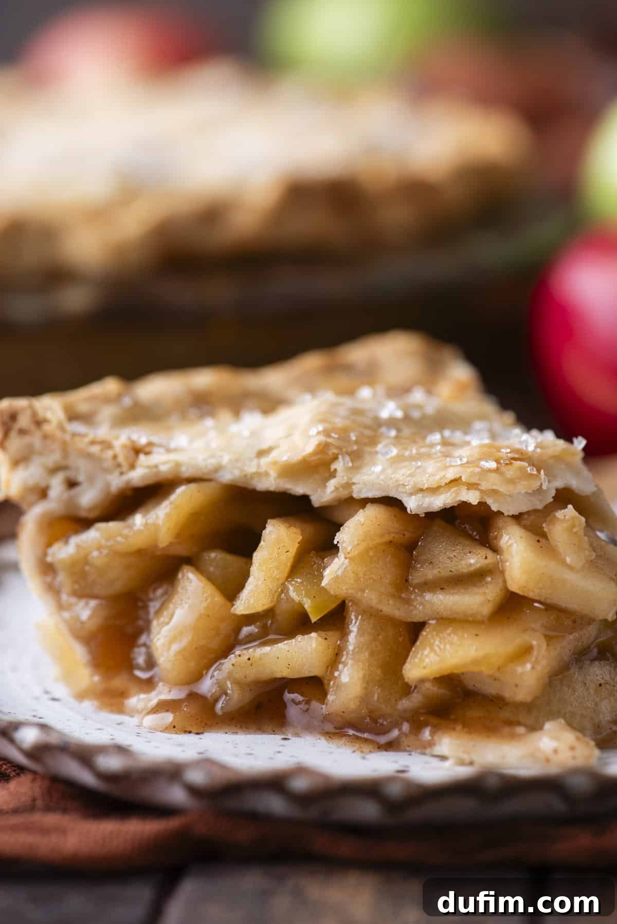 Side view of a perfectly baked slice of apple pie on a small white plate, showcasing the rich filling and golden crust.