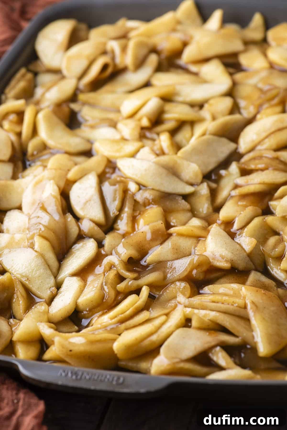 A generous amount of prepared apple pie filling, featuring tender apple chunks and glossy syrup, spread invitingly across a baking sheet.