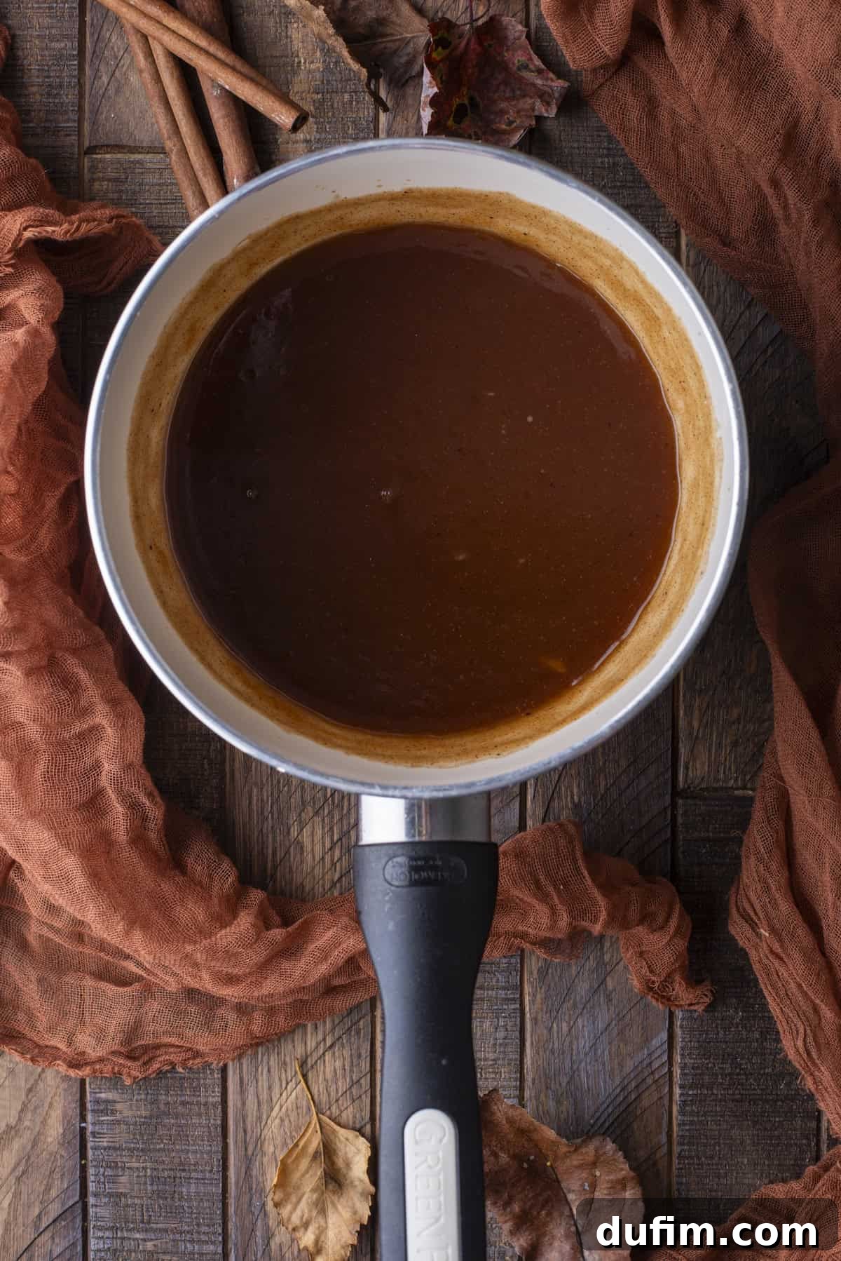 An inviting overhead shot of luscious syrup bubbling gently in a saucepan, surrounded by fragrant cinnamon sticks and vibrant fall foliage.