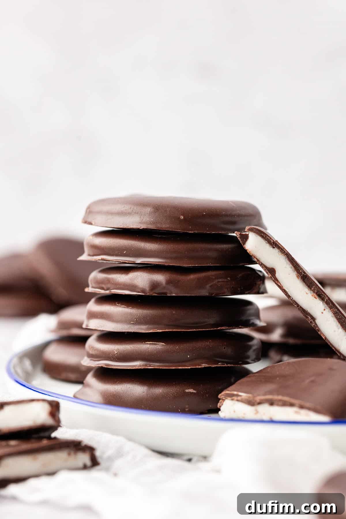Cool & Creamy Homemade Peppermint Patties 2 A stack of perfectly formed peppermint patties on a plate, surrounded by more patties, some cut in halves to reveal the creamy white filling.