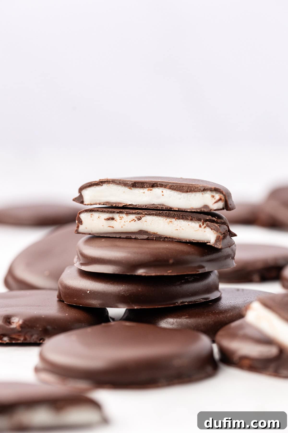 Cool & Creamy Homemade Peppermint Patties 14 A delightful arrangement of scattered and stacked peppermint patties, with two halves prominently displayed on top of the stack, revealing their pristine white centers.