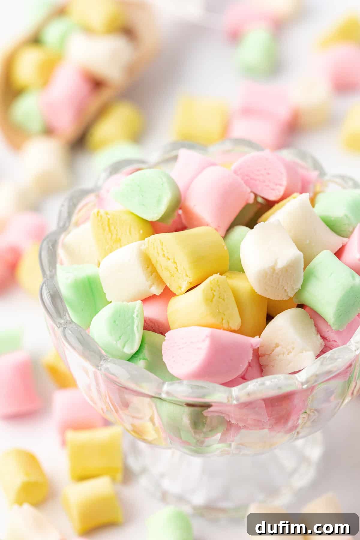 Melt-In-Your-Mouth Butter Mints 2 A small glass trifle dish filled with an assortment of pink, yellow, white, and green butter mints, with more colorful mints scattered around the base.